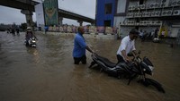Sejumlah warga mendorong kendaraan bermotor saat melewati jalan yang banjir di Ahmedabad, India, Senin (26/8/2024).    