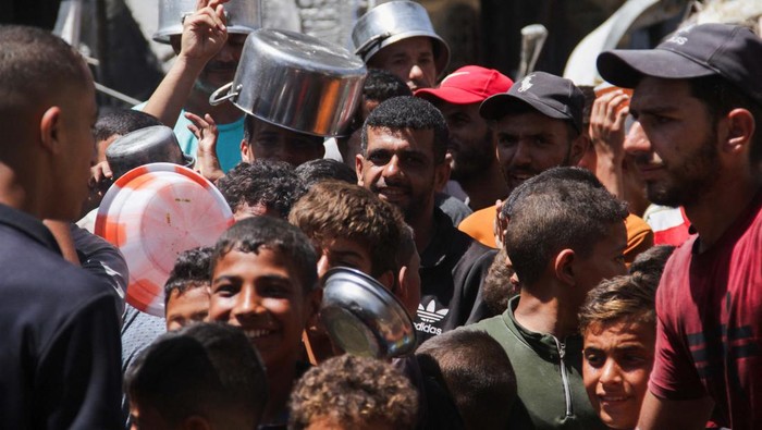 Palestinians gather to receive food cooked by a charity kitchen, amid Israel-Hamas conflict, near the ruins of houses destroyed during the Israeli offensive, in Jabalia in the northern Gaza Strip August 26, 2024. REUTERS/Mahmoud Issa