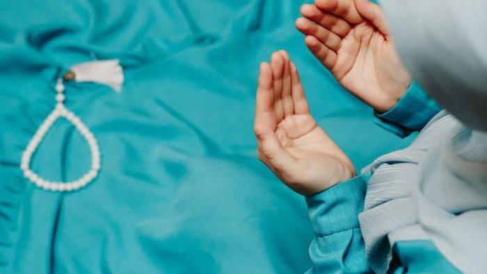 Muslim woman in a headscarf praying and a prayer beads in the background