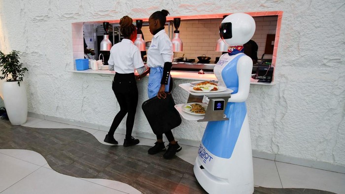 Sensasi Makan di Kafe Robot Kenya Priscilla Muite takes a photograph of Caroline Nyaga as she picks up her meal from a Robotic technology server at the Robot Cafe, the food hub featuring robots that serves customers in Nairobi, Kenya, August 22, 2024. REUTERS/Monicah Mwangi