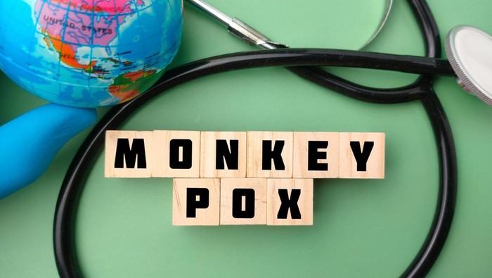 Top view hand holding earth globe and stethoscope with the word MONKEY POX on green background.