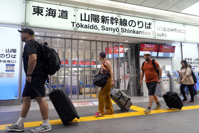 A person has a lunch box outside of the Tokaido and Sanyo Shinkansen bullet trains at Tokyo Station Friday, Aug. 30, 2024, in Tokyo, as its gate was closed due to heavy rains caused by a tropical storm. (AP Photo/Eugene Hoshiko)