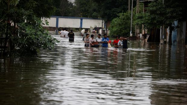 Orang-orang membawa barang-barang mereka untuk menyeberangi jalan yang banjir setelah hujan lebat di Ahmedabad, India, 28 Agustus 2024. (REUTERS/Amit Dave)