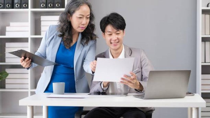 Skilled 50s senior female manager  explaining market research results in graphs to young male employee.