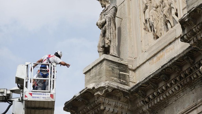 A tourist takes photos of the 315 A.D Arch of Constantine, near the Colosseum, in Rome, Wednesday, Sept. 4, 2024, as workers on site with cranes gather up fragments and secure broken areas of the arch after lightning struck it during a storm Tuesday, Sept. 3, loosening fragments from the ancient Roman structure. (AP Photo/Andrew Medichini)