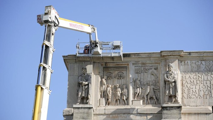 A tourist takes photos of the 315 A.D Arch of Constantine, near the Colosseum, in Rome, Wednesday, Sept. 4, 2024, as workers on site with cranes gather up fragments and secure broken areas of the arch after lightning struck it during a storm Tuesday, Sept. 3, loosening fragments from the ancient Roman structure. (AP Photo/Andrew Medichini)