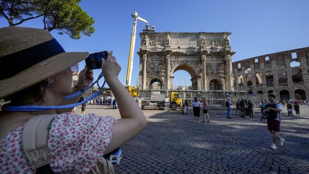 A tourist takes photos of the 315 A.D Arch of Constantine, near the Colosseum, in Rome, Wednesday, Sept. 4, 2024, as workers on site with cranes gather up fragments and secure broken areas of the arch after lightning struck it during a storm Tuesday, Sept. 3, loosening fragments from the ancient Roman structure. (AP Photo/Andrew Medichini)