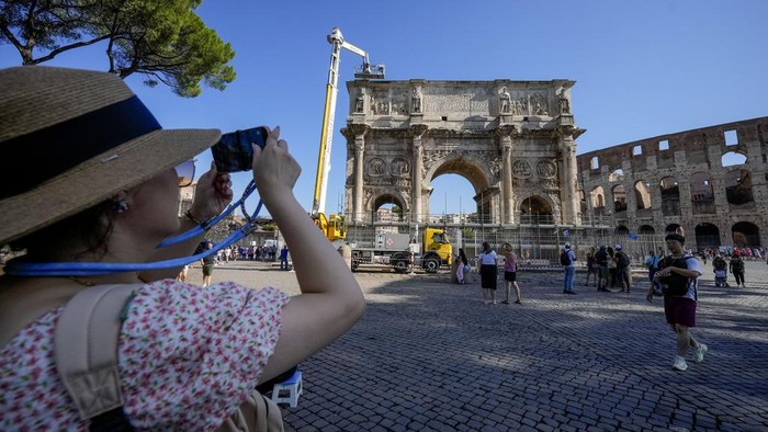 Duh, Bangunan Romawi Kuno di Italia Rusak Disambar Petir A tourist takes photos of the 315 A.D Arch of Constantine, near the Colosseum, in Rome, Wednesday, Sept. 4, 2024, as workers on site with cranes gather up fragments and secure broken areas of the arch after lightning struck it during a storm Tuesday, Sept. 3, loosening fragments from the ancient Roman structure. (AP Photo/Andrew Medichini)