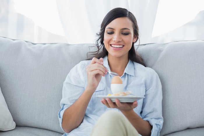 Cheerful brunette eating egg in her living room