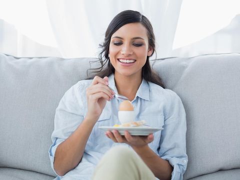Ilustrasi diet tiongkok atau makan telur Cheerful brunette eating egg in her living room
