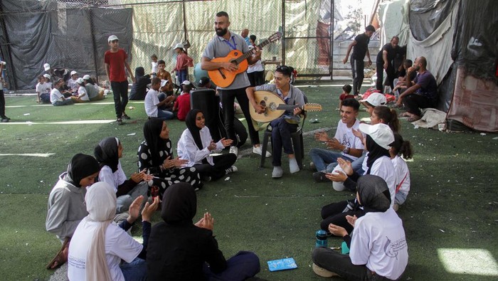 Palestinian teenager Youssef Saad sits on the rubble of his house as he plays oud to bring joy to children, amid Israel-Hamas conflict, in Jabalia refugee camp in the northern Gaza Strip September 2, 2024. REUTERS/Mahmoud Issa