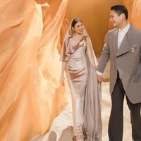 Studio dibuat seperti gurun pasir dengan palet warna camel. Clarissa tampak mengenakan gaun bertudung warna emas metalik rancangan desainer Stella Rissa. Sang suami, Anthony Tjipto, mengenakan jaket dengan lapel asimetris dipadu celana abu-abu gelap dan kemeja putih. Foto: Instagram/@clarissatanoe @solemnstudios