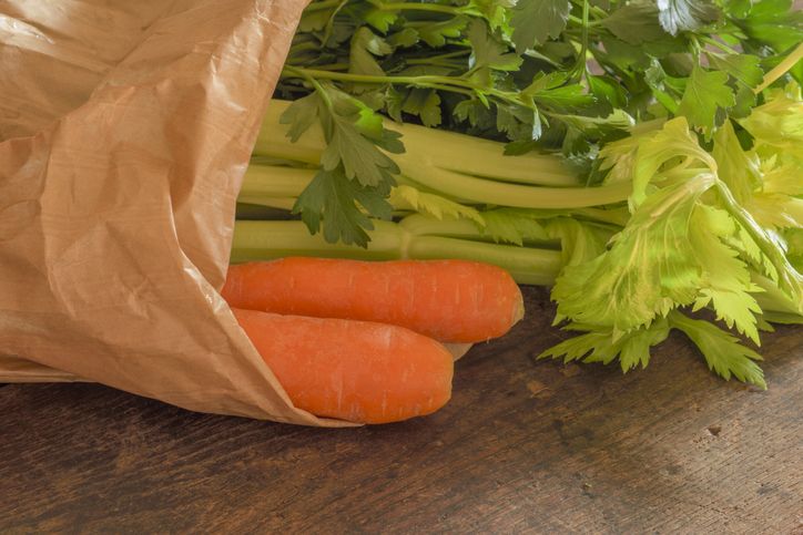 Carrots, celery and parsley in a paper grocery bag on a rustic old wood tabletop