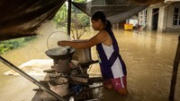 Salah satu ibu rumah tangga tetap memasak meski tengah dilanda banjir.