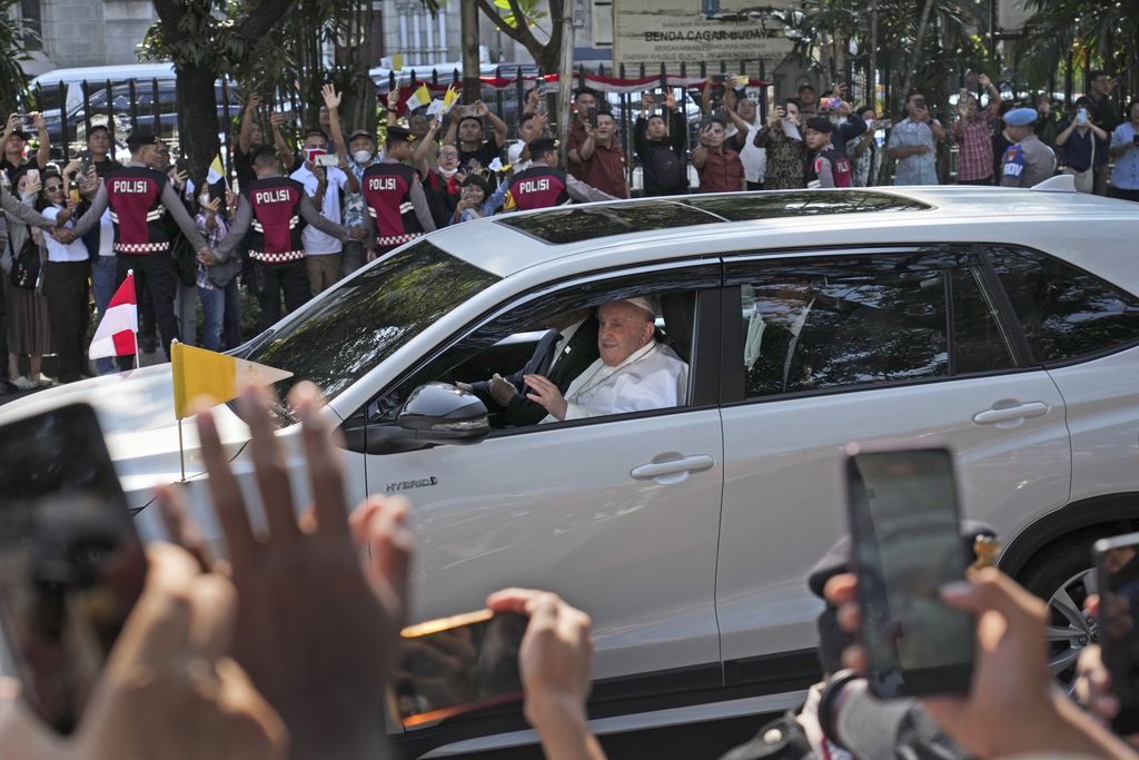 Orang-orang yang berdiri di pinggir jalan melambaikan tangan dan mengambil foto saat Paus Fransiskus tiba di Masjid Istiqlal untuk pertemuan antaragama, di Jakarta, Indonesia, Kamis, 5 September 2024. (AP Photo/Achmad Ibrahim)