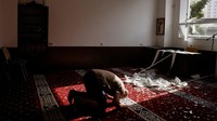 Imam sedang salat di depan tumpukan pecahan kaca di salah satu ruangan masjid.  