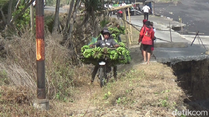Warga Lumajang nekat melewati jalan penghubung Kecamatan Pasirian-Tempursari yang ambles imbas abrasi pantai.