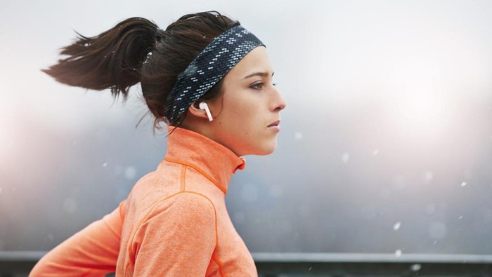 Shot of a fit young woman using wireless earphones during her workout on a rainy day outside