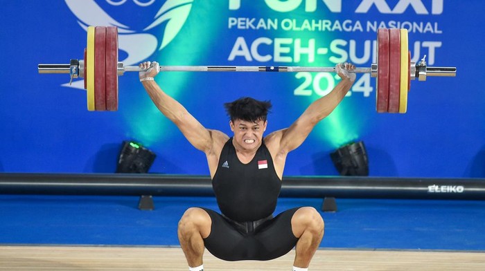 Lifter Banten Rizki Juniansyah melakukan angkatan clean and jerk saat angkat besi kelas 89 kilogram putra PON XXI Aceh-Sumut 2024 di GOR Seuramoe Angkat Besi Harapan Bangsa, Banda Aceh, Aceh, Sabtu (7/9/2024). Rizki Juniansyah berhasil meraih emas sekaligus memecahkan rekor nasional dengan total angkatan 360 kg melampaui rekor sebelumnya yakni 337 kilogram atas nama Muhammad Zul Ilmi. ANTARA FOTO/Budi Candra Setya/pras.