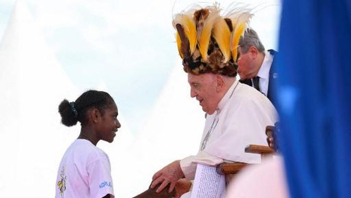 This handout picture taken and released on September 8, 2024 by the Vatican Press Office shows Pope Francis, seen wearing a traditional headdress, interacting with a youth during a meeting with Catholic faithful of the diocese of Vanimo in front of Holy Cross Cathedral in Vanimo, Papua New Guinea, on September 8, 2024. (Photo by Handout / VATICAN MEDIA / AFP) / RESTRICTED TO EDITORIAL USE - MANDATORY CREDIT 