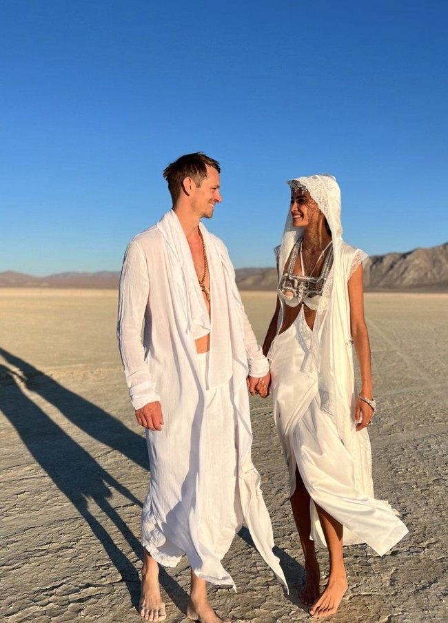 Yang menarik perhatian publik adalah penampilan keduanya yang tanpa alas kaki. Tidak mengenakan gaun pengantin bervolumen, Kelly menggunakan gaun putih dengan detail potongan di bagian perut dan hiasan perak di bagian atasnya, lengkap dengan kerudung yang dihiasi renda tipis yang menjuntai hingga nyaris menyentuh tanah. Sementara itu, Joel mengenakan kemeja putih tipis dan celana panjang, tampak santai dan serasi dengan tema upacara tersebut. Foto: dok. Instagram @kellygale