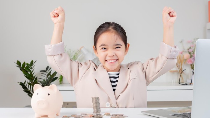 Asian little cute girl wearing a cream suit analyzing coins concept of finance and investment in white room