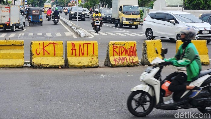 Pengendara melintas di samping tulisan 'JKT Anti Ridwan Kamil' dan JKT Anti RK', di Jl Bungur Besar, Jakarta, Selasa (10/9/2024). Tulisan liar tersebut berada di beton barrier tanpa keterangan siapa yang bertanggungjawab. Seperti diketahui, reaksi penolakan atas Ridwan Kamil mengemuka usai ia mendaftar sebagai pasangan calon Bersama Suswono dalam Pilgub Jakarta.