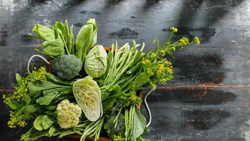 Market fresh green leaf vegetables in an old wooden crate on an old wooden table. Vegetables include, broccoli, cauliflower, cabbage, spring greens, bok choy, spinach and choy sum.