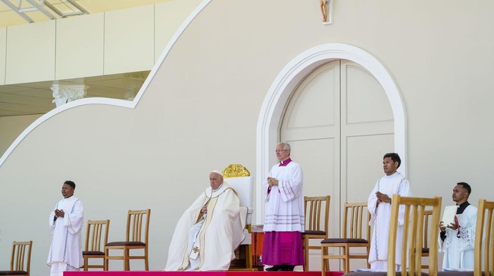 Momen Paus Fransiskus Pimpin Misa Nazar di Timor Leste Archbishop of Dili Cardinal Virgilio do Carmo da Silva, right, protects Pope Francis, wearing an East Timor traditional scarf, from the sun with an umbrella with the colors of the Vatican flag as he arrives to preside over a votive mass of the Blessed Virgin Mary Queen in Tasitolu, some 8 kilometers west of Dili, East Timor, Tuesday, Sept. 10, 2024. Pope Francis presides over a mass in a seaside park on the same field where St. John Paul II celebrated a historic liturgy during East Timor's fight for independence from Indonesian rule. (AP Photo/Gregorio Borgia)