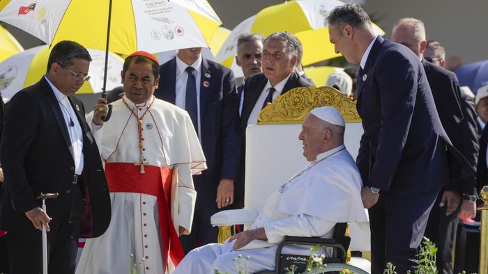 Archbishop of Dili Cardinal Virgilio do Carmo da Silva, right, protects Pope Francis, wearing an East Timor traditional scarf, from the sun with an umbrella with the colors of the Vatican flag as he arrives to preside over a votive mass of the Blessed Virgin Mary Queen in Tasitolu, some 8 kilometers west of Dili, East Timor, Tuesday, Sept. 10, 2024. Pope Francis presides over a mass in a seaside park on the same field where St. John Paul II celebrated a historic liturgy during East Timor's fight for independence from Indonesian rule. (AP Photo/Gregorio Borgia)