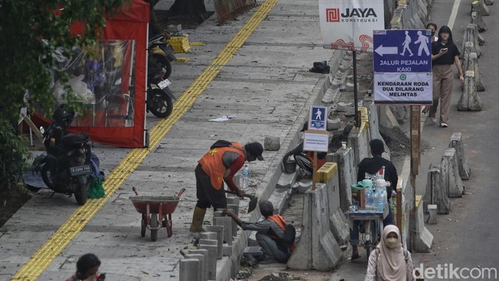 Para pejalan kaki melintas di samping proyek jalur pedestrian di Jl Rasuna Said, Jakarta, Kamis (12/9/2024). Sebagian mulai terlihat hasilnya, sebagian lagi masih menyisakan pekerjaan karena kendala teknis seperti jaringan serat kabel bawah tanah yang membuat pekerjaan berjalan lebih lambat.