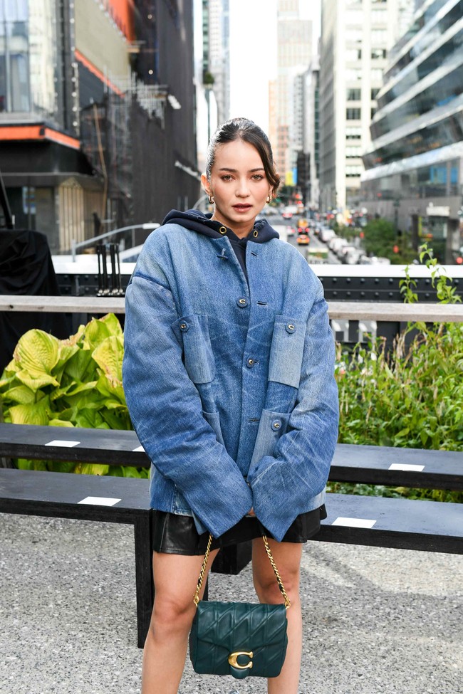 Enzy Storia mengenakan tank top hitam dengan luaran berupa jaket oversized berbahan denim, serta rok mini kulit. Padanan busananya memberi kesan bold, edgy dan androgini. Foto: dok. Coach