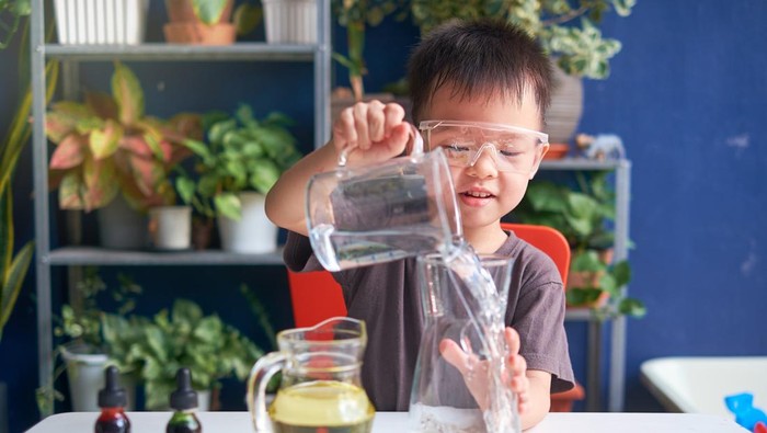 Happy little Asian school kid studying science, making DIY Lava Lamp Science Experiment with oil, water and food coloring, Kid-friendly fun and easy science experiments at home concept