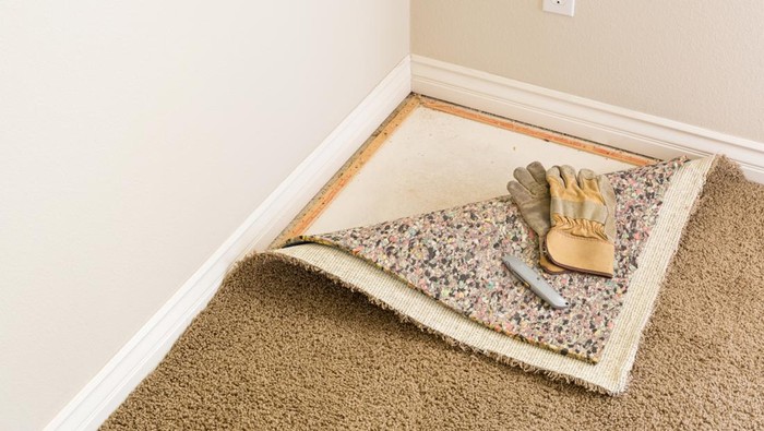 Construction Gloves and Utility Knife On Pulled Back Carpet and Pad In Room.