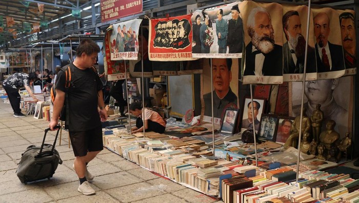 A vendor attends to a customer next to images and statues depicting late Chinese chairman Mao Zedong, at the secondhand books section of Panjiayuan antique market in Beijing, China August 3, 2024. REUTERS/Florence Lo