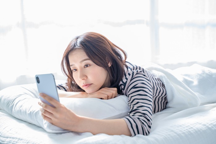 A woman falling asleep staring at a smartphone screen in bed.