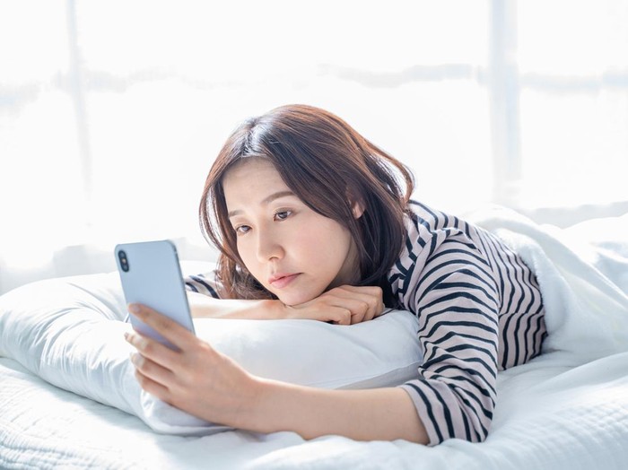 Ilustrasi insomnia A woman falling asleep staring at a smartphone screen in bed.