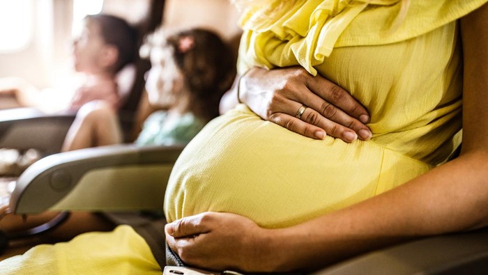 Close up of unrecognizable expecting mother caring for her unborn baby while traveling by airplane.