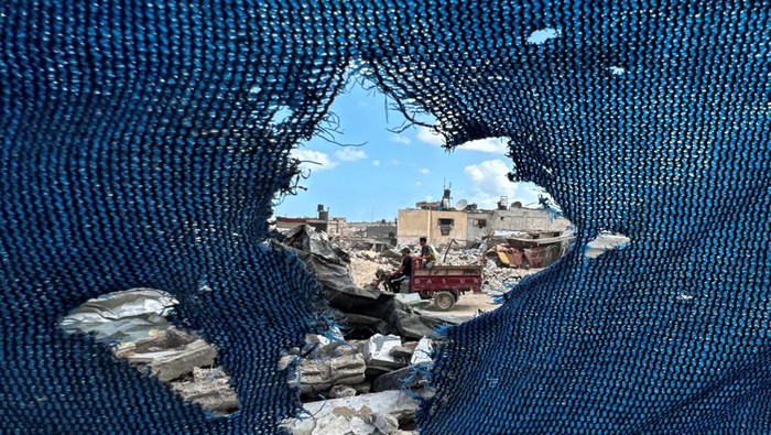 Palestinians, seen through a torn tent, ride a motorized vehicle past the rubble, amid the Israel-Hamas conflict, in Khan Younis, in the southern Gaza Strip, September 16, 2024. REUTERS/Mohammed Salem     TPX IMAGES OF THE DAY