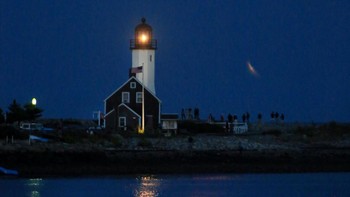 Pemandangan ini menyajikan kombinasi menawan antara bulan yang tampak lebih besar dan lebih terang dari biasanya, dengan siluet mercusuar yang berdiri kokoh di tepi laut. REUTERS/Lauren Owens