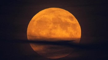 Supermoon berwarna seperti labu muncul di antara awan di atas Samudra Atlantik di lepas pantai Camden, Maine, Amerika Serikat, Selasa (17/8). Foto: AP/Petros Karadjias