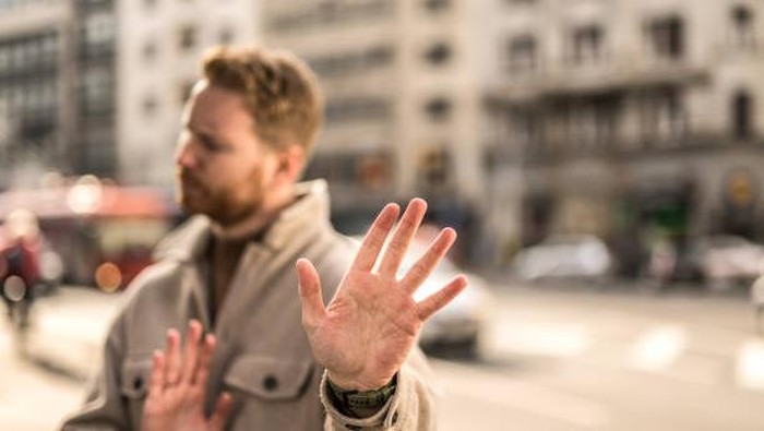 Young man standing on city street and making refusal gestures. Focus on foreground.
