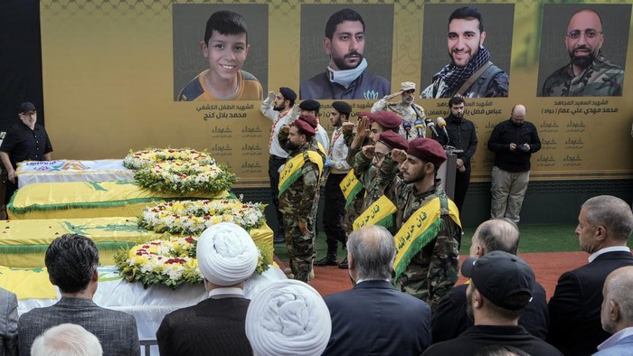 Momen Pemakaman Korban Ledakan Pager di Lebanon Hezbollah fighters salute as they stand next to the coffins of four victims who were killed Tuesday after their handheld pagers exploded, during their funeral procession in the southern suburb of Beirut, Lebanon, Wednesday, Sept. 18, 2024. (AP Photo/Bilal Hussein)