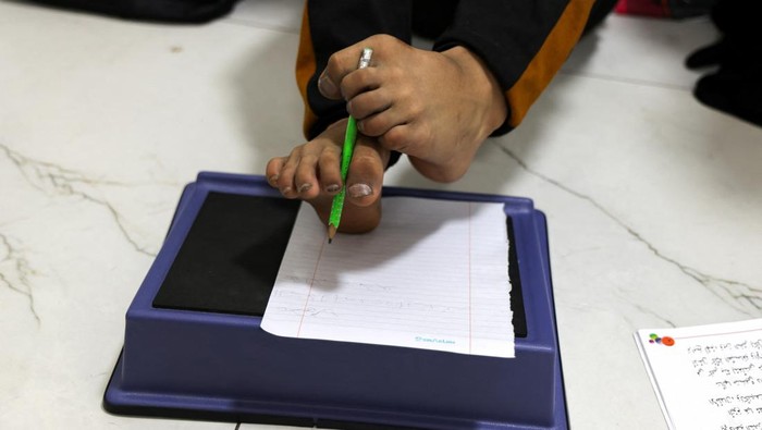 Mahmoud Ajjour, an injured child evacuated from Gaza, sits at home with his mother as she teaches him to write using his feet, in Doha, Qatar, September 11, 2024. REUTERS/Ibraheem Abu Mustafa
