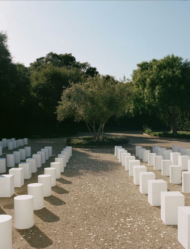 Terinspirasi fashion show Jacquemus yang simple dan elegan, bangku-bangku tamu pun ditata minimalis berwarna putih, tanpa dekorasi rumit menuju ‘altar’. Hanya beberapa taburan kelopak bunga putih untuk memberi nuansa romantis. Foto: Instagram/@normanandblake @charlieputh @puthbrooke