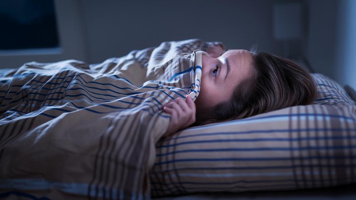 Scared woman hiding under blanket. Afraid of the dark. Unable to sleep after nightmare or bad dream. Awake in the middle of the night in bedroom at home.  Monster under the bed or in closet.