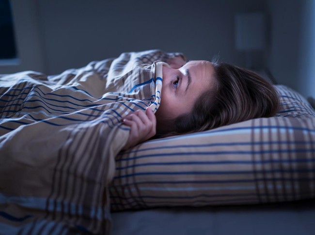 Scared woman hiding under blanket. Afraid of the dark. Unable to sleep after nightmare or bad dream. Awake in the middle of the night in bedroom at home.  Monster under the bed or in closet.