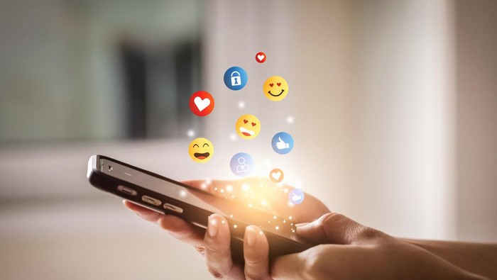 Young man using smartphone sending emojis. Mobile smartphone sending text messages emoji emoticon.