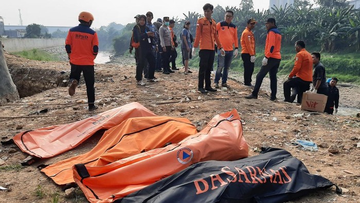 Sejumlah petugas BPBD Kota Bekasi dan polisi berdiri dengan latar depan kantong-kantong  berisi tujuh jenazah laki laki yang ditemukan mengambang di Kali Bekasi, Pondok Gede Permai, Jatiasih, Kota Bekasi, Minggu (22/9/2024). Kepolisian masih menyelidiki penyebab kematian tujuh orang tersebut. ANTARA FOTO/Rezas Ale/app/foc.