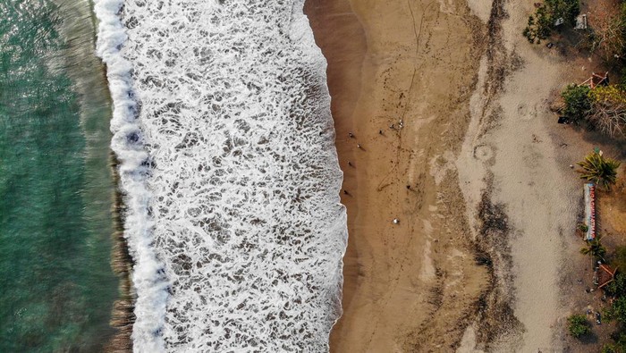 Foto udara pengunjung bermain air di Pantai Ungapan di sekitar Jalur Lintas Selatan, Malang, Jawa Timur, Minggu (22/9/2024). Keberadaan Jalur Lingkar Selatan (JLS) sejauh 50 kilometer di pesisir Malang yang sudah ada sejak tahun 2016, kini membawa dampak positif bagi perkembangan sektor pariwasata di kawasan tersebut di antaranya telah resmi dibuka sekitar 33 pantai yang dikelola oleh kelompok masyarakat setempat bersama Perhutani sehingga dapat menunjang perekonomian di wilayah itu. ANTARA FOTO/Muhammad Mada/Spt.